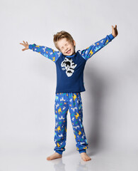 Awaken blond kid boy in pyjamas with african animals pattern and map print stands stretches in the morning.