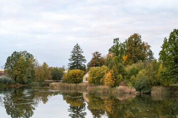 Fototapeta na wymiar Cloudy autumn view with small lake with old house between trees.