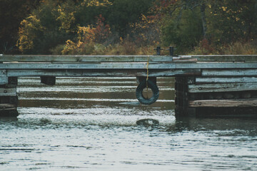 bridge with a tire hanging off the bottom with fall trees in the background
