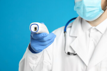 Doctor holding non contact infrared thermometer against light blue background, focus on hand....