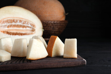 Pieces of delicious honey melon on black wooden table, closeup