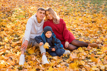 Young family for a walk. Man, woman, child sit on the ground on a warm autumn day.