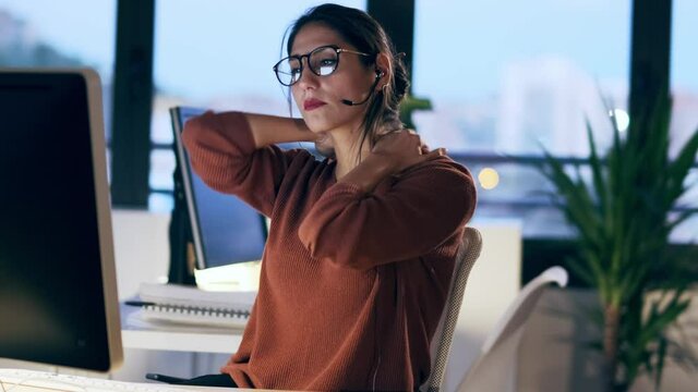 Shot of tired business woman with back pain looking uncomfortable while working with computers sitting in the office.