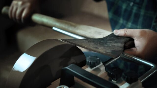 Asian man sharpening axe on a grinder