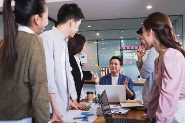 Focus on asian man(boss or manager)standing in group brainstorm meeting in office.Businesspeople discussing with paperwork for business plan,Corporate of modern colleague
