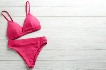 Beautiful pink bikini on white wooden background, top view. Space for text