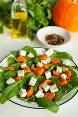Bright autumn salad with pumpkin, spinach and feta cheese on a light concrete background. Diet healthy food. View from above. A place for text.