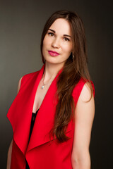 Studio portrait of a young woman in a red suit on a dark background.