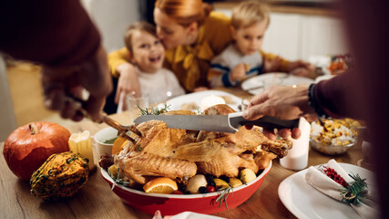 Close-up of man carving Thanksgiving turkey during family dinner at home.