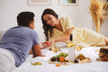 Obraz na płótnie Canvas Happy couple with wine and tasty food imitating picnic at home