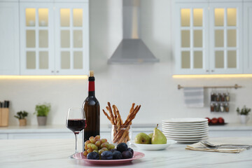Red wine and snacks on white table in modern kitchen. Space for text