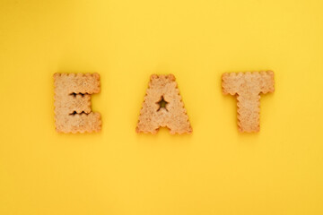Cookie alphabet symbols E A T on top view with yellow background