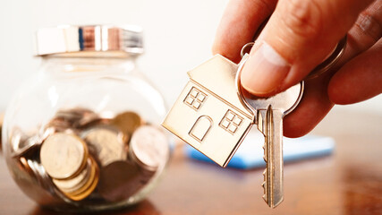 House keychain on hand with background bowl glass carry coins on the table , banking concept .