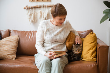 A happy senior woman with Pet cat sitting on a sofa indoors  at home.
