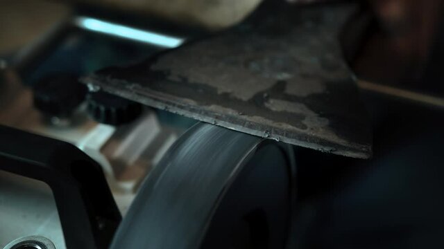 Asian man sharpening axe on a grinder