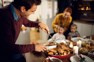 Happy man carving meat during Thanksgiving dinner at dining table.
