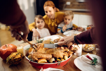 Close-up of man carving roasted turkey during Thanksgiving dinner.