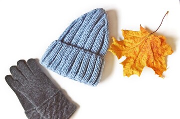 Blue woolen gloves, blue knitted hat and yellow maple leaf. Warm clothes for fall and winter season isolated on a white background