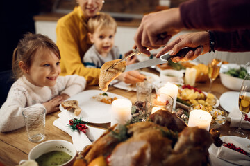 Close-up of father serving turkey meat during Thanksgiving dinner at dining table.