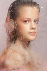 Young beautiful woman with perfect skin behind a glass with raindrops on pink background