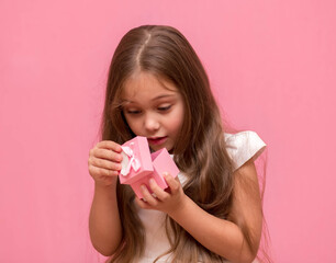 little girl joyful opens a gift box on a pink background