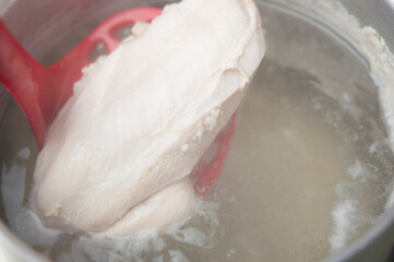 A healthy wholesome chicken breast broth is cooked on a stove in a saucepan