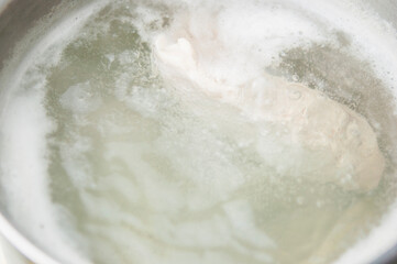 A healthy wholesome chicken breast broth is cooked on a stove in a saucepan