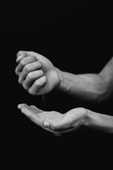 black and white photograph of hands with sand on a black background