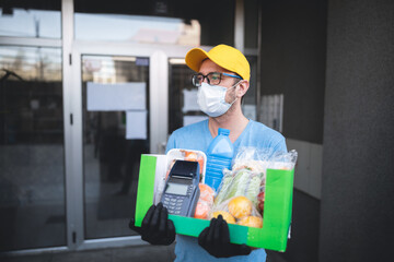 Delivery guy with protective mask holding box / bag with groceries and POS for contactless payment.