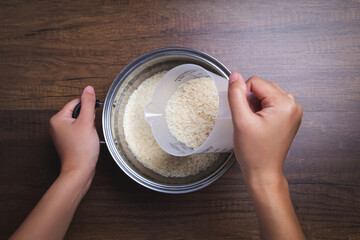 Woman hand is pouring jasmine rice into pot. Using measuring glass. on wooden table.