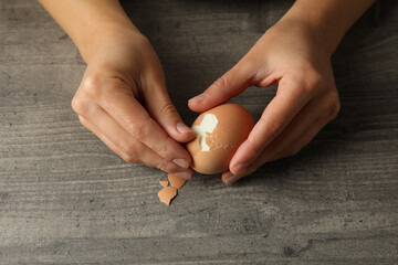 Woman peeling boiled egg on gray background