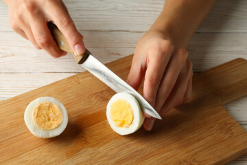 Woman cuts boiled egg on board on white wooden background