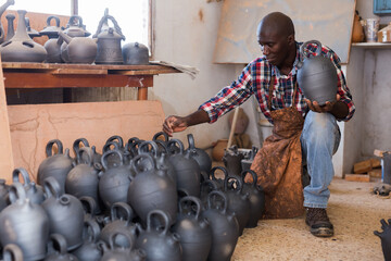Positive african potter enjoying work, checking ceramic products in pottery studio
