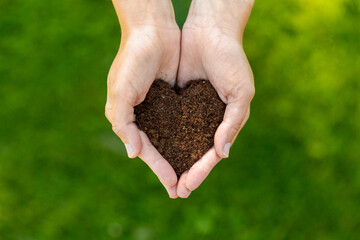 gardening, environment and people concept - cupped hands holding soil in shape of heart at summer...