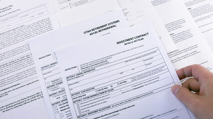 Obraz premium Conceptual composition. Pension savings. Man puts on the table Blank form Investment contract 401 k or 457 plan, blank form Utah retirement system 401 k and Personal 401k plan. Close-up