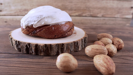 Cinnamon bun with yoghurt cream on a wooden stand standing on a wooden background next to nuts