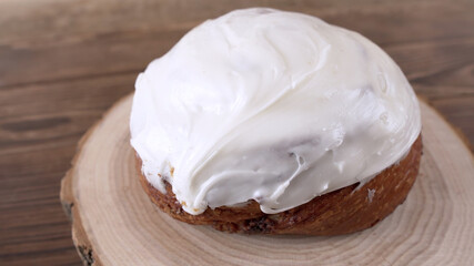 Cinnamon bun with yoghurt cream on a wooden stand standing on a wooden background. Close-up