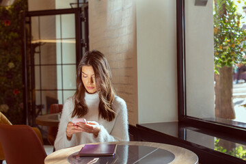 Beautiful young woman texting on the smartphone in the cafe bar