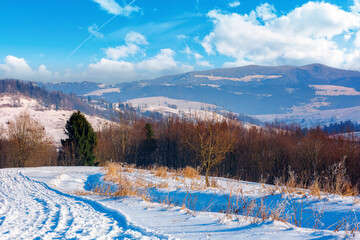 winter countryside on a sunny day. forest on snow covered hills. mountain ridge in the distance beneath a bright blue sky with clouds