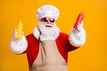 Fototapeta na wymiar White grey beard hair santa claus in chef headwear cook x-mas christmas party snack hold mustard tomato sauce bottle wear sunglass apron isolated bright shine color background