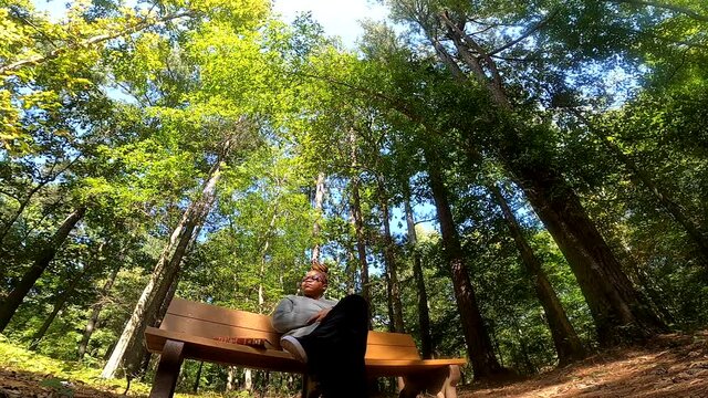 Low angle of Black woman wearing glasses enjoying daydreaming being in Nature with her bible laying next to her