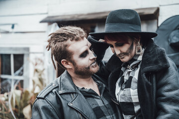 Fototapeta premium Scary love couple,man,woman.Family,mother,father celebrating halloween.Terrifying black skull face makeup. Witch costumes, stylish images.Horror,fun at children's party in barn on street.Hats,jackets
