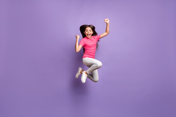 Full length body size photo of jumping high cute little girl celebrating win cheering shouting smiling isolated on purple color background