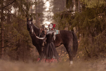 Young woman dressed as mexican symbol of day of the dead posing in forest with horse