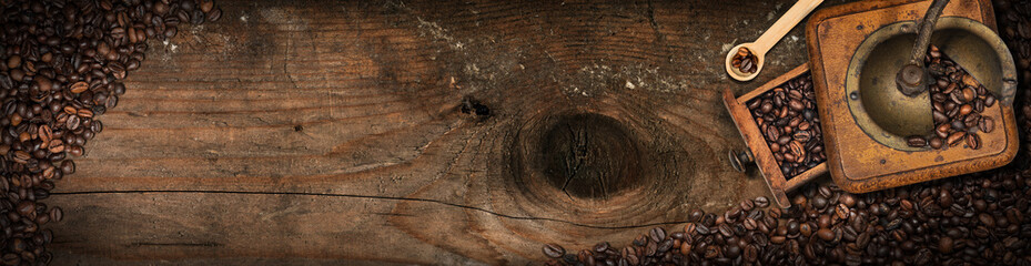 Old manual coffee grinder on a wooden background with roasted coffee beans and copy space.