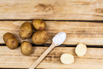 Wooden spoon with starch and a bunch of potatoes on a wooden background.