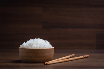 Fototapeta na wymiar Cooked jasmine rice in wooden bowl with chopsticks on wooden table. Thai Jasmine rice.
