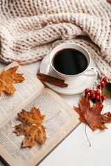 Autumn morning coffee. Cup of coffee and book on a plaid against the background of autumn leaves. Still life concept.