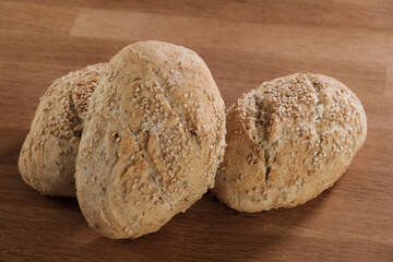Drei traditionell gebackene Sesambrötchen / Frühstücksbrötchen auf einem rustikalen Holztisch
