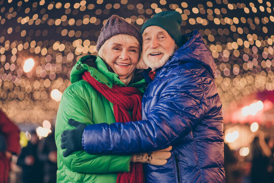 Photo of dream two people old man woman couple enjoy x-mas christmas advent eve time date hug embrace under evening illumination outside